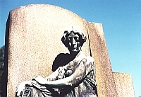 Standbild engelhafter Frau vor einem Grabstein